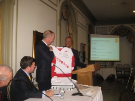 GMC主席约翰·丹尼尔斯(右)在2014年11月10日周一在大学俱乐部举行的GMC月度会议上向加拿大冰球迷、BMO哈里斯金融首席执行官比尔·道恩赠送了一件威斯康星獾队曲棍球球衣，该球衣由教练迈克·埃夫斯签名。