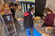 2022年3月16日，购物者在饥饿任务小组移动市场排队结账，该市场停在密尔沃基高地花园公寓外。移动市场是一家车轮上的杂货店，由马利基的Piggly Wiggly和饥饿特别工作组经营，他们在密尔沃基县各地走访那些获得新鲜健康食品有限的社区，但移动市场的前期和持续成本创造了一个具有挑战性的商业模式。(Coburn Dukehart / Wisconsin Watch)